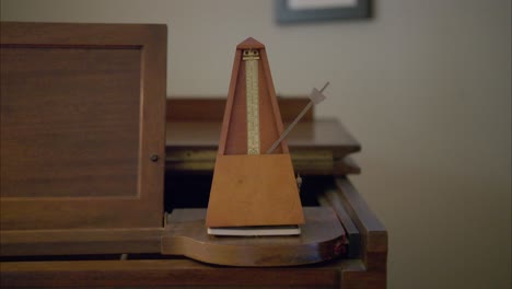 un metrónomo antiguo de madera marca 60 latidos por minuto balanceando un peso hacia adelante y hacia atrás una vez por segundo en la parte superior de un viejo piano