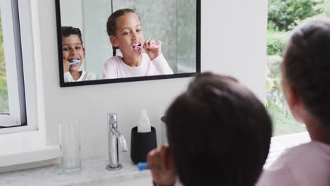 hermano y hermana bi-raciales felices cepillándose los dientes en un baño soleado, cámara lenta