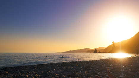 Sunset-at-Playa-de-las-Alberquillas,-Andalusia,-Spain,-with-silhouette-of-people-swimming-at-the-sea