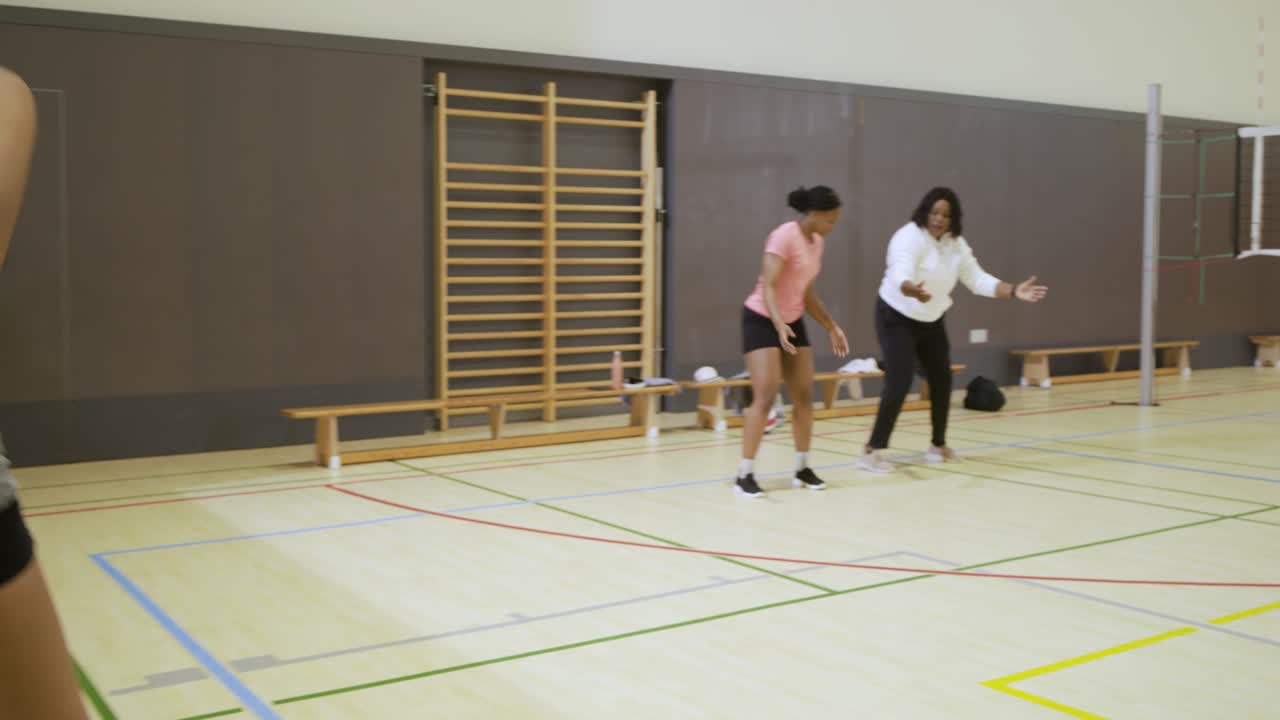 Mature African American coach cueing pink player practicing bump with ball in gym, copy space