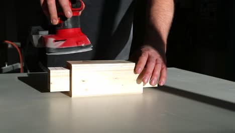 a woodworker sands a piece of wood with a random orbital sander in slow motion