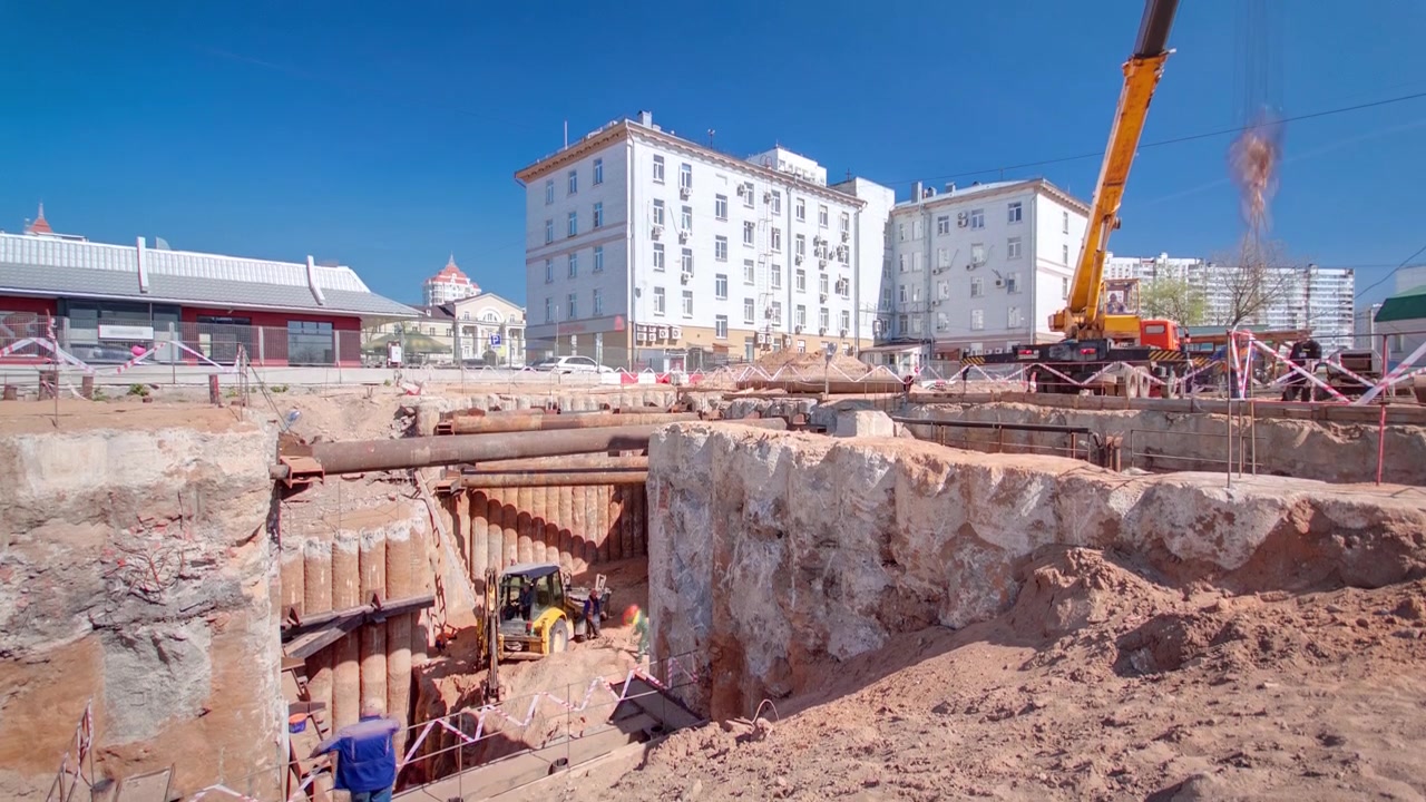 Ein großer, riesiger Graben-Schacht-Tunnel Zeitraffer mit Kran und Bagger. Verstärkungsstrukturen aus dicken Eisenrohren von Trägern und Strukturen an der Baustelle der U-Bahn-Linie