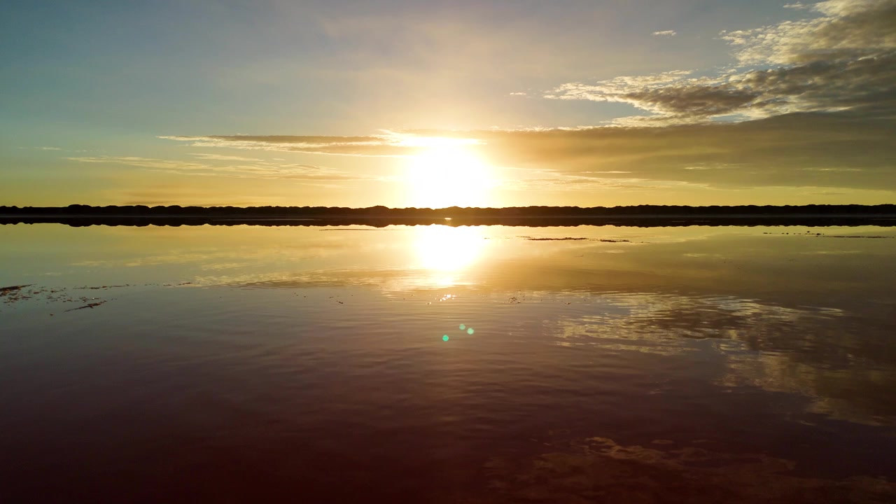 Low aerial shot pulling back over a salt pond revealing a rising sun. Walvis Bay, Namibia