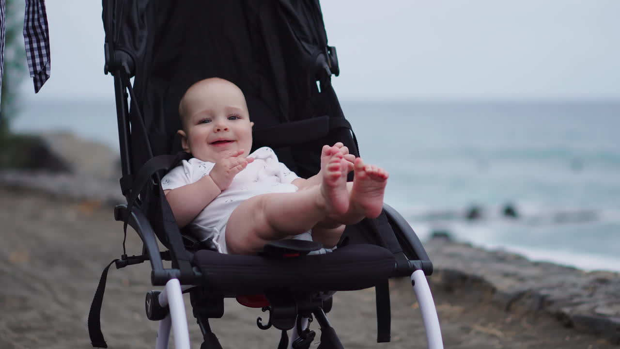 Resting in a stroller on the sandy beach, the baby peacefully gazes at the sea waves, captivated by the vastness of the horizon. The late summer evening by the sea brings pure enjoyment