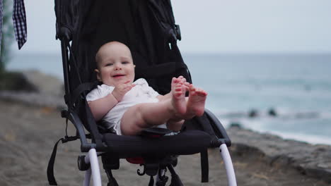 Resting-in-a-stroller-on-the-sandy-beach,-the-baby-peacefully-gazes-at-the-sea-waves,-captivated-by-the-vastness-of-the-horizon.-The-late-summer-evening-by-the-sea-brings-pure-enjoyment