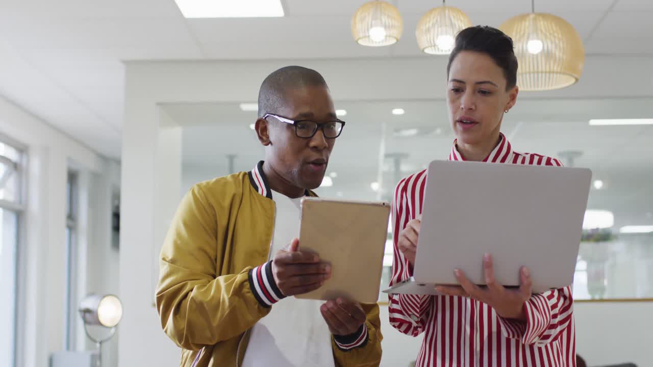 Diverse male and female colleagues using laptop and tablet, having business talk in office