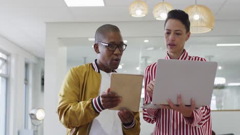 diverse male and female colleagues using laptop and tablet, having business talk in office