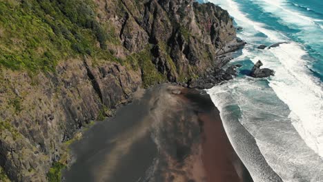 aerial view of clear unpolluted paradise beach with waves crash on the rock cliff scenario, comans track, karekare, new zealand