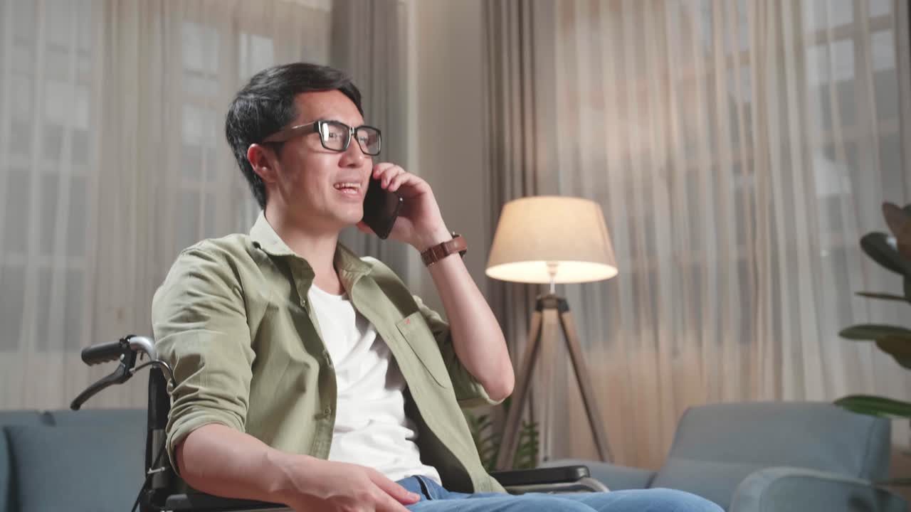 Asian Man Sitting In A Wheelchair And Talking On Phone At Home