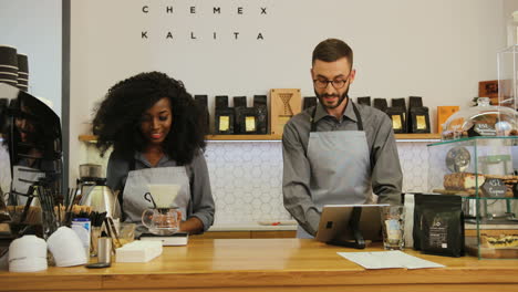 hombre caucásico con barba y joven barista afroamericana trabajando en una cafetería moderna
