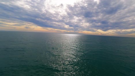 scenic fpv aerial flying over the mediterranean sea as the sun sets behind the clouds