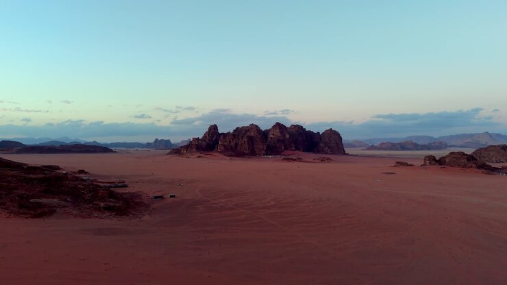 Vista aerea cinematografica di una remota valle desertica in Giordania, che mette in risalto la luce blu fredda e le profonde tonalità arancioni della sabbia all'alba o al tramonto, clip video girata con drone nel deserto del Wadi Rum