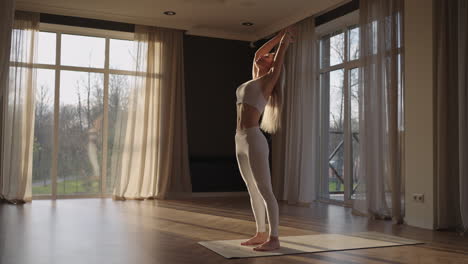 a young woman in white sportswear is stretching with a large hall with large windows in a slow-motion scheme the sun's rays shine through the window. healthy lifestyle healthy morning