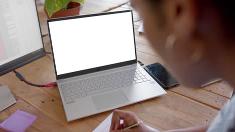 mujer de negocios afroamericana usando una computadora portátil con espacio para copiar y tomando notas en la oficina, cámara lenta