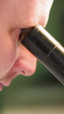 una vista de cerca de un hombre mirando atentamente a un microscopio, centrándose en su cara y el ocular, con un fondo borroso