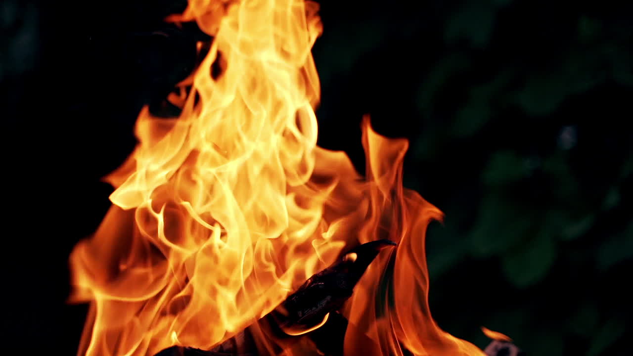 Bright flame with orange and red colors in the darkness. Vivid fire sparkles at night outdoors. Close-up.