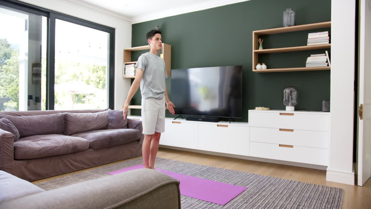 Focused biracial man practicing yoga standing in living room, copy space, slow motion