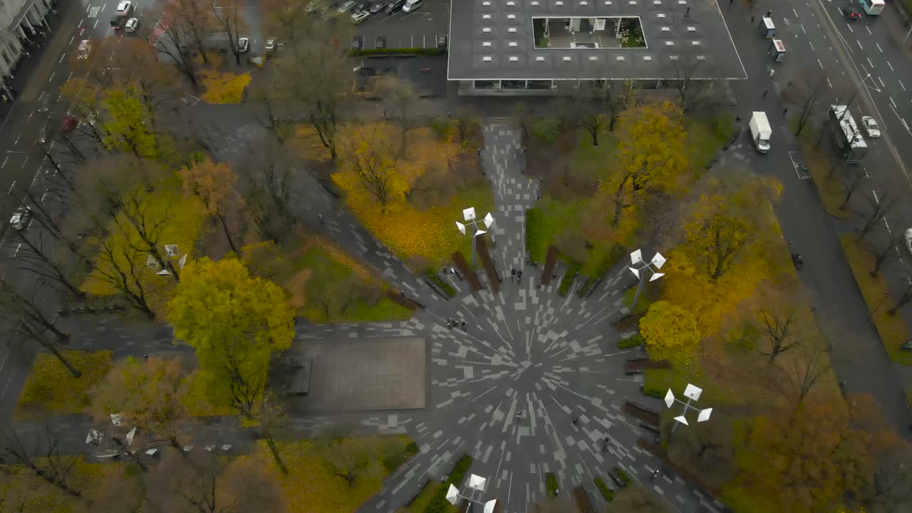 Aerial drone video revealing a large modern autumn time Tammsaare park in Estonia central city with cars, vehicles, trams and buses driving around on the damp and wet streets at cloudy day