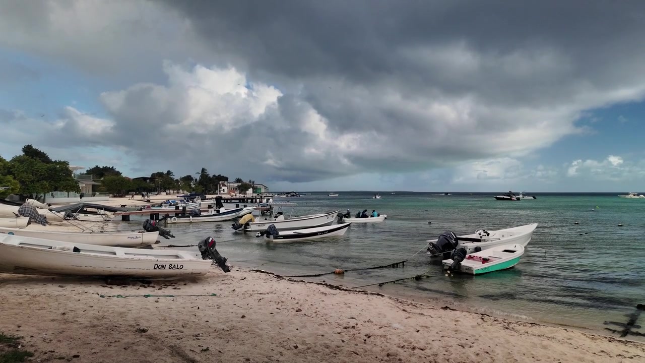 Piccole barche da pesca ancorate lungo una spiaggia caraibica sotto drammatiche nuvole temporalesche a Los Roques, Venezuela.