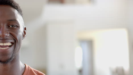 Half-face-of-happy-african-american-man-standing-and-laughing-in-sunny-living-room,-slow-motion