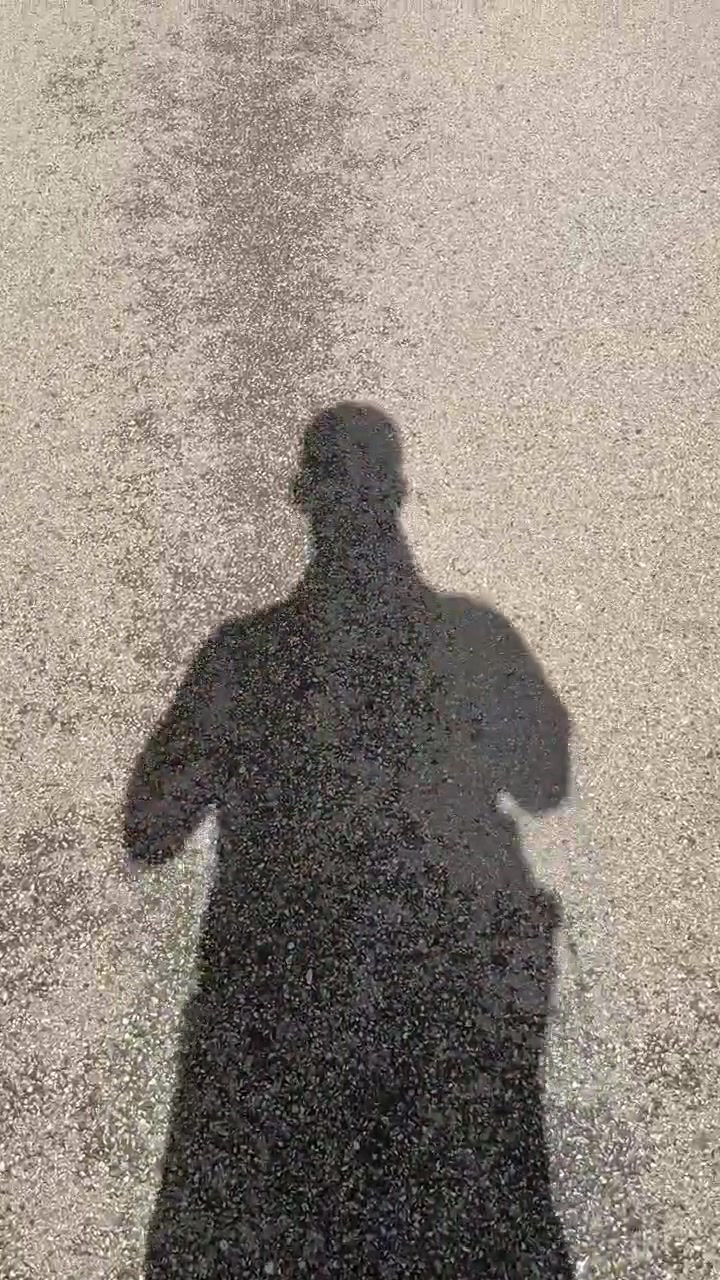 Ein langer menschlicher Schatten geht zügig auf dem Bürgersteig