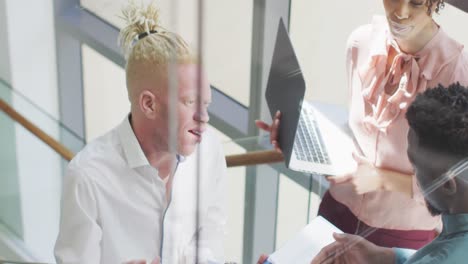 Smiling-diverse-business-people-discussing-with-laptop-and-documents-in-creative-office