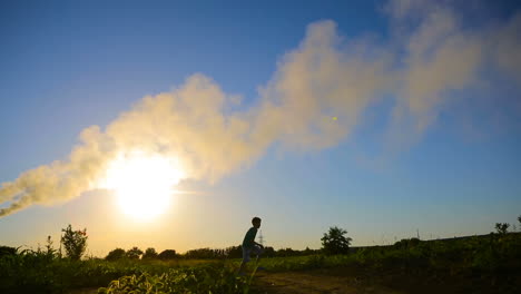 young boy flying a paper plane. boy playing in grass with paper airplane near smoky pipes