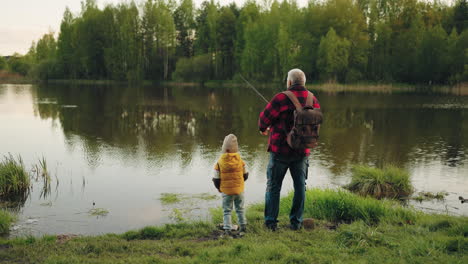 Opa-Und-Kleines-Kind-Angeln-Am-Ufer-Eines-Schönen-Teiches-Im-Wald,-Rückansicht,-Wochenende-In-Der-Natur