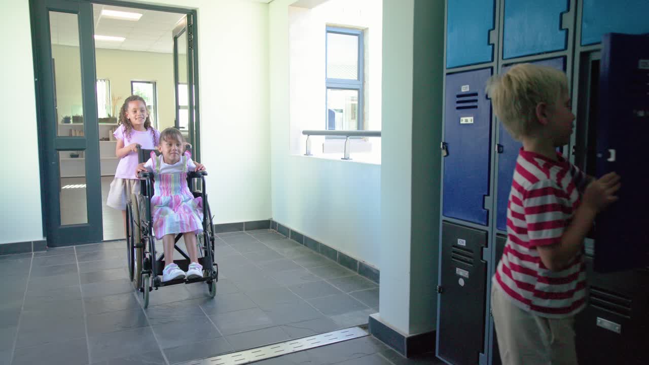 Bambini di diverse origini entrano in un corridoio, un ragazzo prende uno zaino dagli armadietti blu e aiuta un amico in sedia a rotelle.