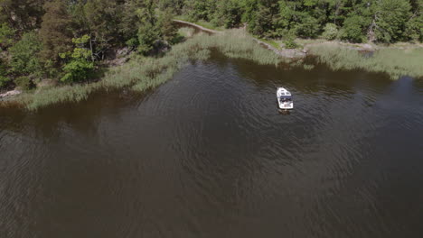 Drone-circling-luxury-motor-boat,-anchored-in-calm-bay,-aerial,-Sweden