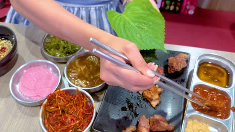 hands preparing korean bbq with vibrant side dishes in a bangkok setting. bright lighting highlights the colorful ingredients and meticulous arrangement