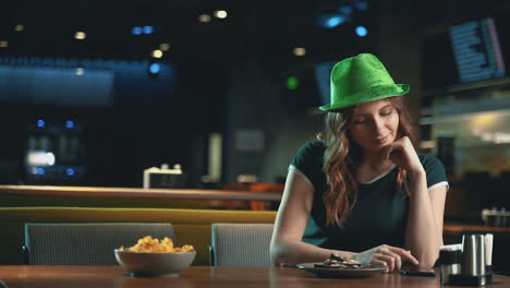 mujer muy joven usando una aplicación con el teléfono inteligente y usando un sombrero verde irlandés