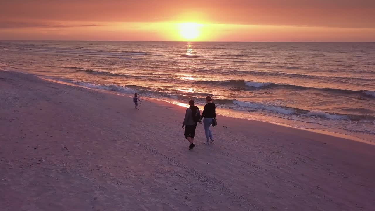 Parents Walking With a Small Child on a Beach at Sunset. Happy Family Enjoying a Walk on a Beach. Sunset Beach Walk Drone Footage.