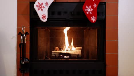 plano general de troncos ardiendo en una chimenea con medias navideñas de copos de nieve rojas y blancas colgando encima