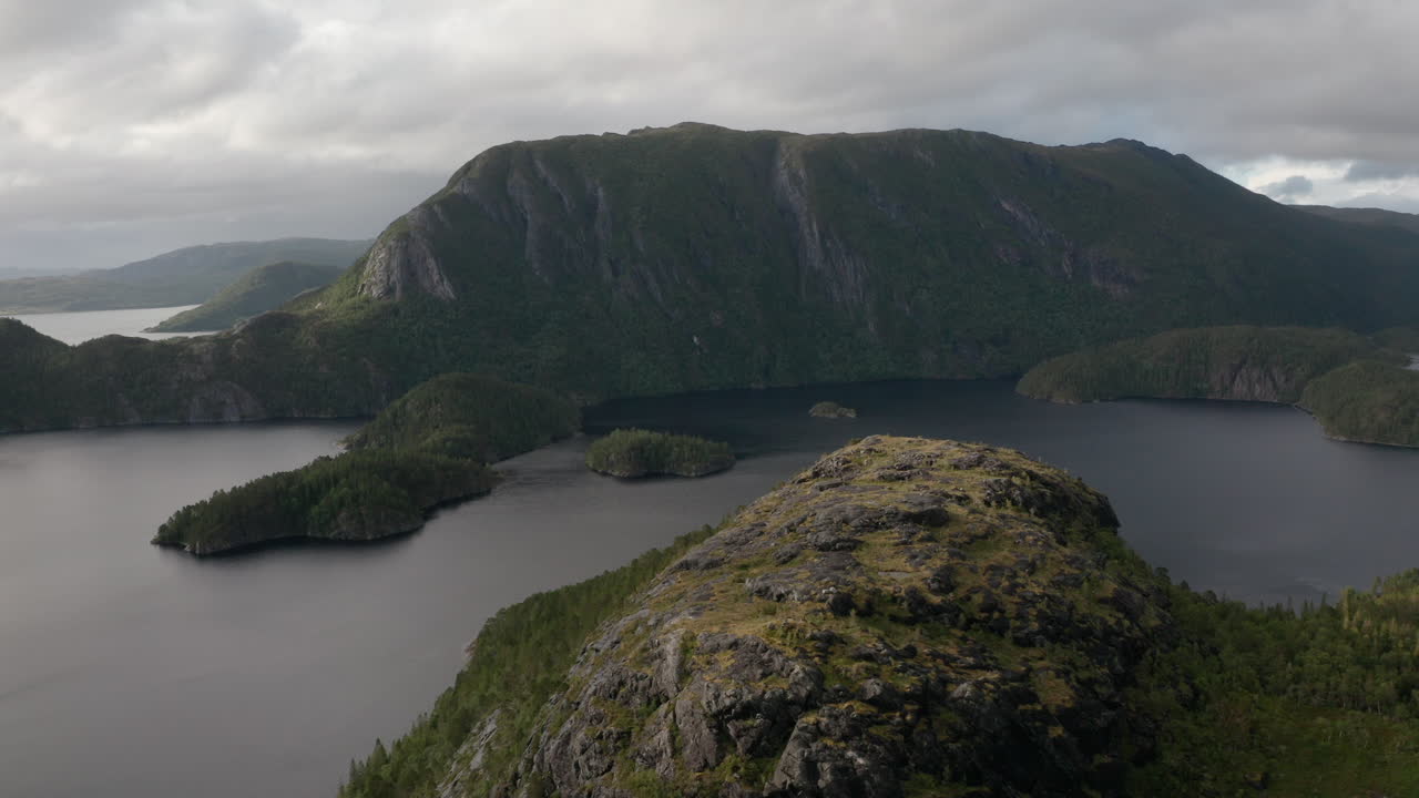 Slow drone flight moving away from rugged cliffside with dark fjord and dramatic mountainous terrain