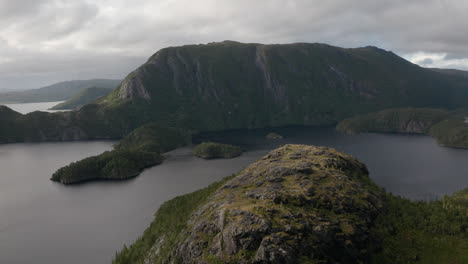 slow drone flight moving away from rugged cliffside with dark fjord and dramatic mountainous terrain