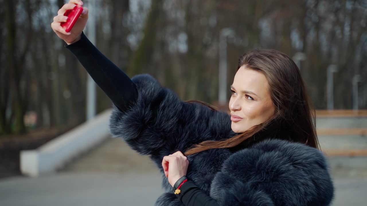 Girl with smartphone in hand. Lifestyle portrait of young positive woman making selfie in park