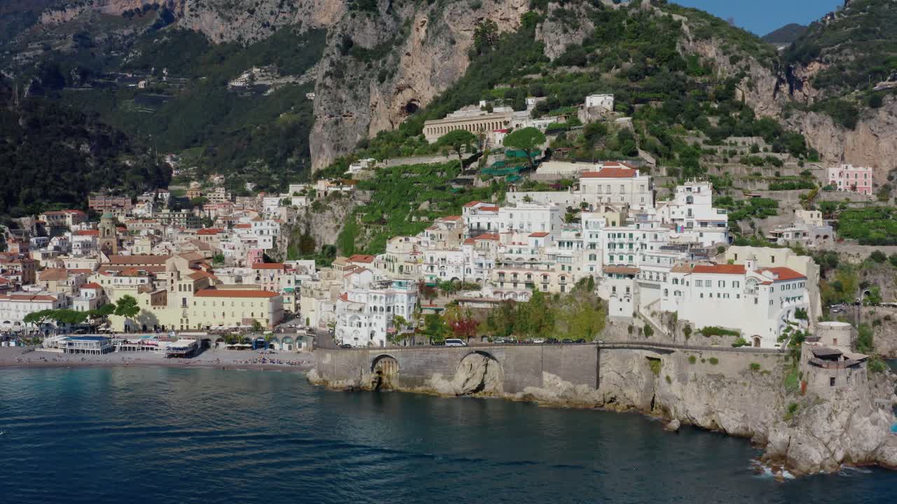 Panorama aereo con drone di una città costiera della Costiera Amalfitana a picco sul mare, affacciata sulle acque turchesi del Mediterraneo in una luminosa giornata di sole. Destinazione UNESCO, Italia.