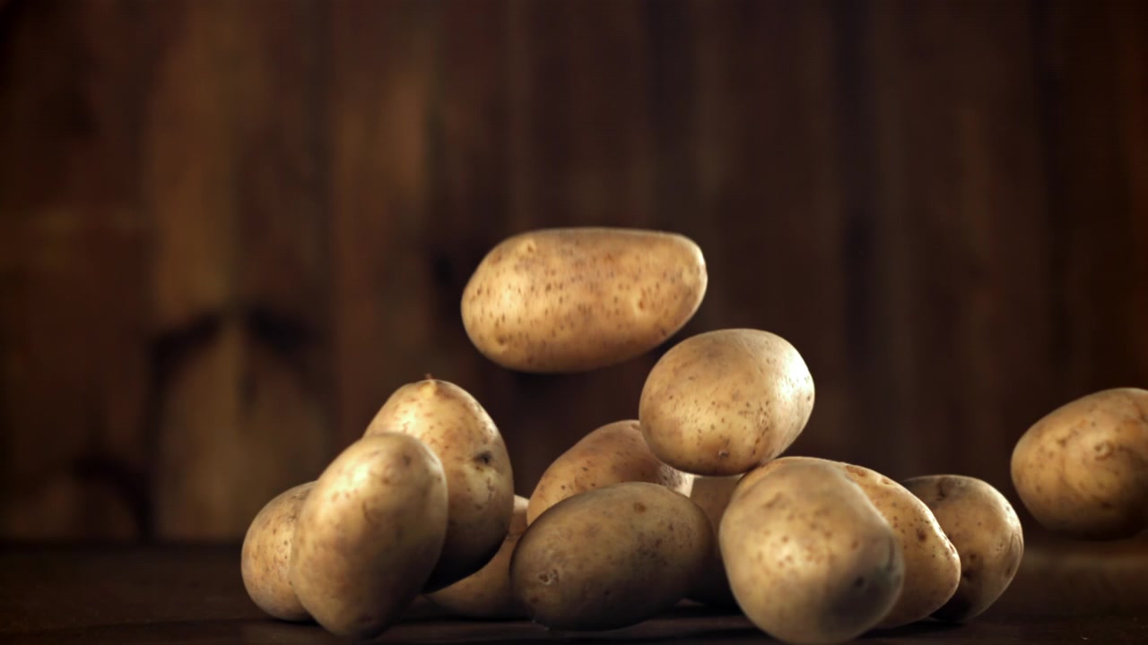 Patate fresche e crude che cadono su una superficie di legno rustica al rallentatore