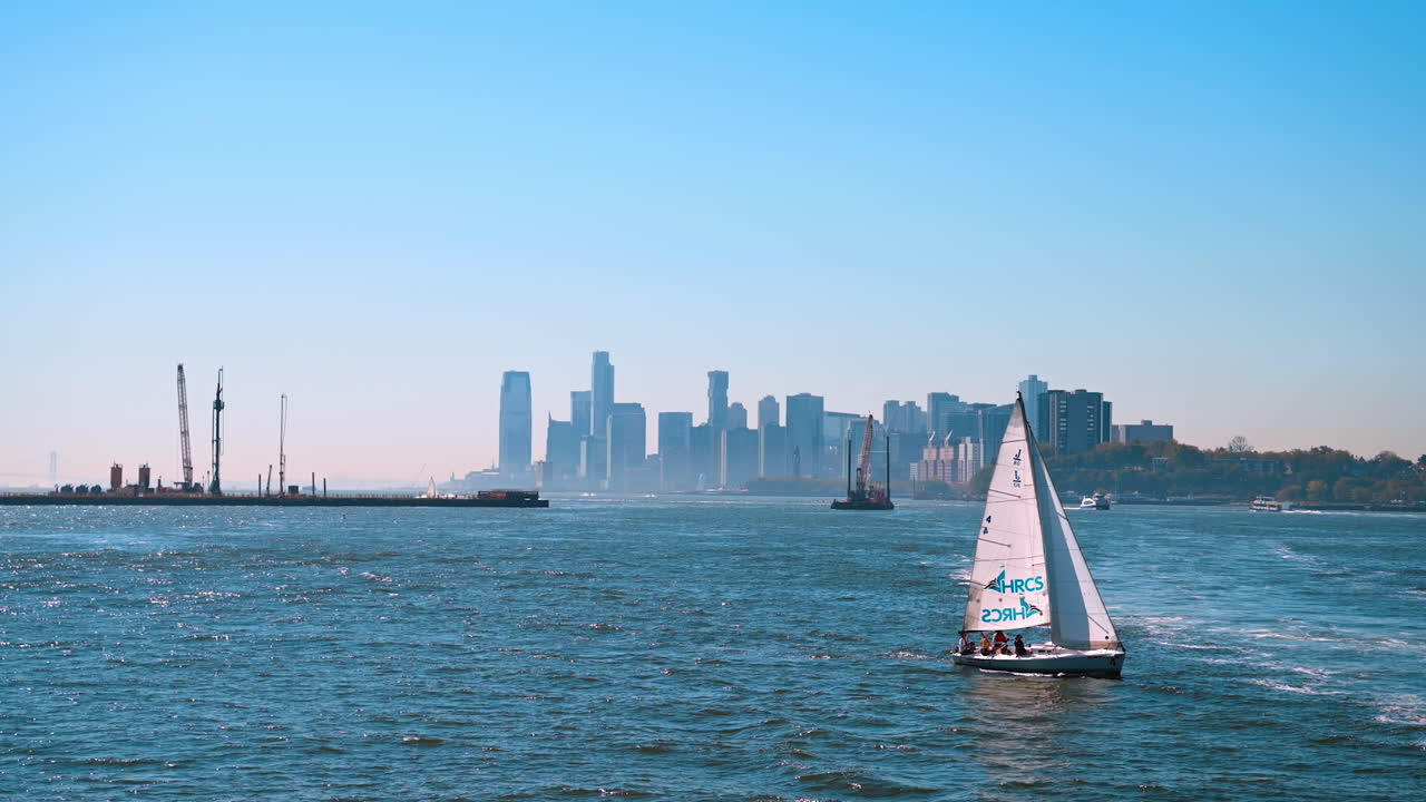 New York, USA, 9 August 2025: Sailboat on Hudson River with Jersey City skyline view. A sailboat glides along the Hudson River with the modern skyline of Jersey City under a clear blue sky