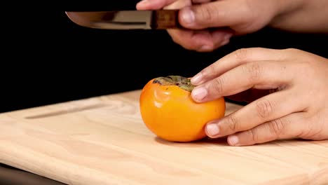close-up of hands carefully handling and slicing a persimmon on a wooden board with a knife.