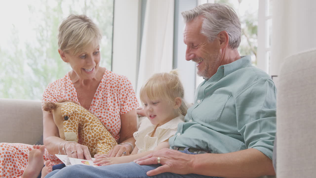 집에서 손녀와 함께 소파에 앉아 함께 책을 읽고 있는 할아버지와 할머니