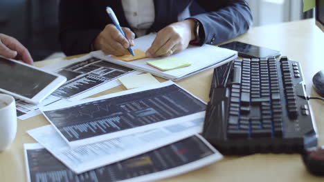 dos comerciantes analizando diagramas financieros y escribiendo en notas adhesivas