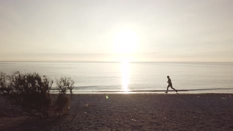 young runner man training on beautiful sunset at beach. drone tracking