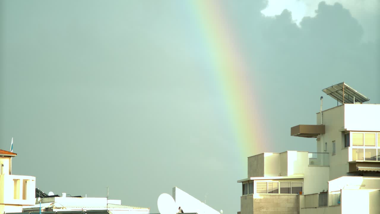 이스라엘의 도시 건물 위에 움직이는 무지개 불빛, 미끄러지는 구름, 어두운 파란 하늘, 지붕 위의  ⁇ 빛, 비가 오는 날씨, 중동 텔 아비브, 소니 4k 비디오