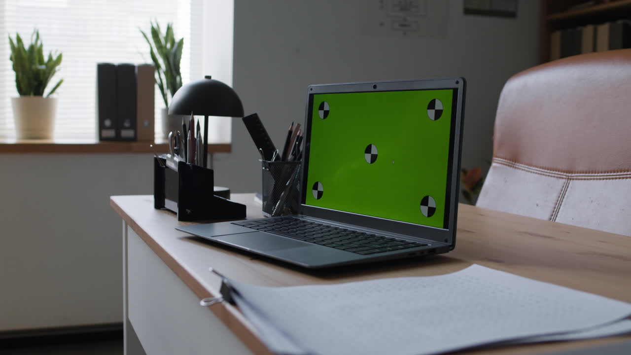 Laptop with Green Screen on a Wooden Desk in an Office