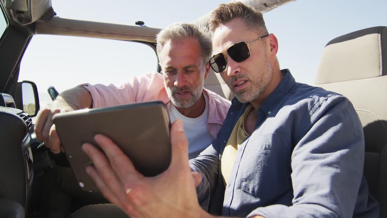 白人ゲイの男性カップルが ⁇ 晴れた日にタブレットを使って車に座っています