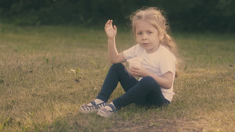 La-Niña-Come-Yogur-Sabroso-Sentado-En-El-Césped-A-Cámara-Lenta