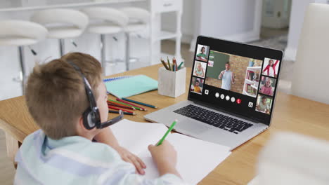 schoolboy using laptop for online lesson at home, with diverse teacher and class on screen