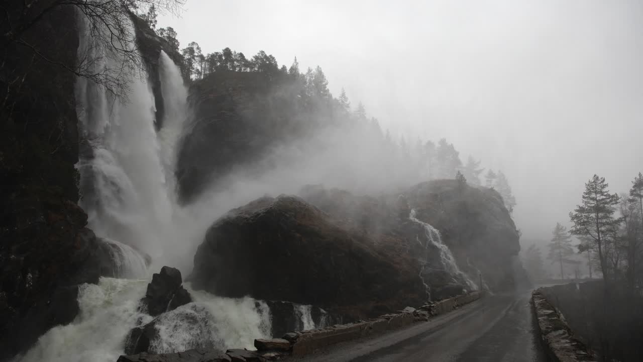 Close view of bridge and road wet from mist and flooding near Hesjedalsfossen. Waterfall overflows during heavy rainstorm in Western Norway